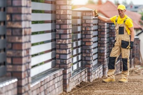 Fence contractor inspecting a finished masonry and metal fence